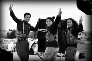 Image of three YPJ militiawomen waving